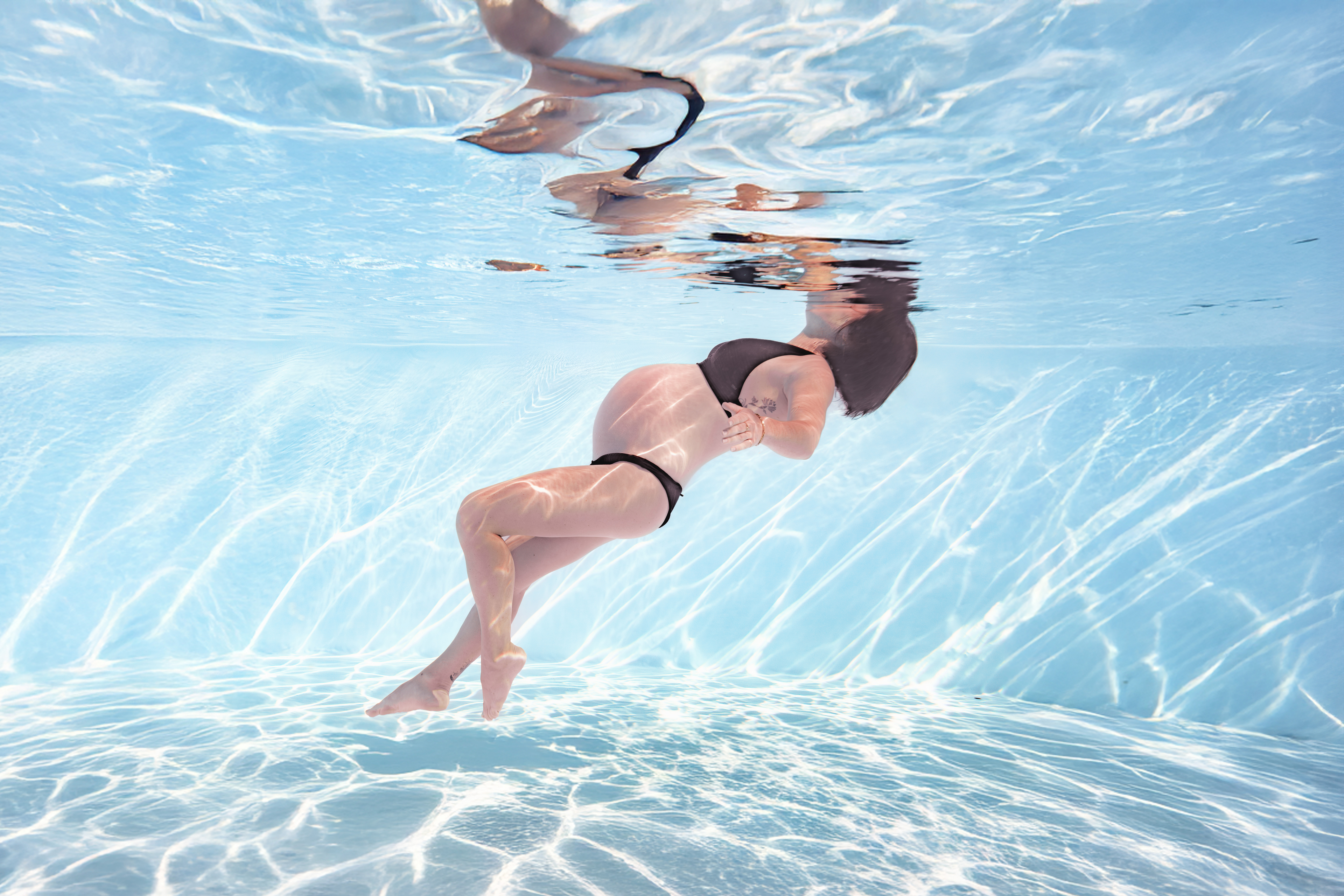Femme enceinte sous l'eau enveloppée d'un tissu rouge flottant dans une piscine — séance grossesse aquatique Landes