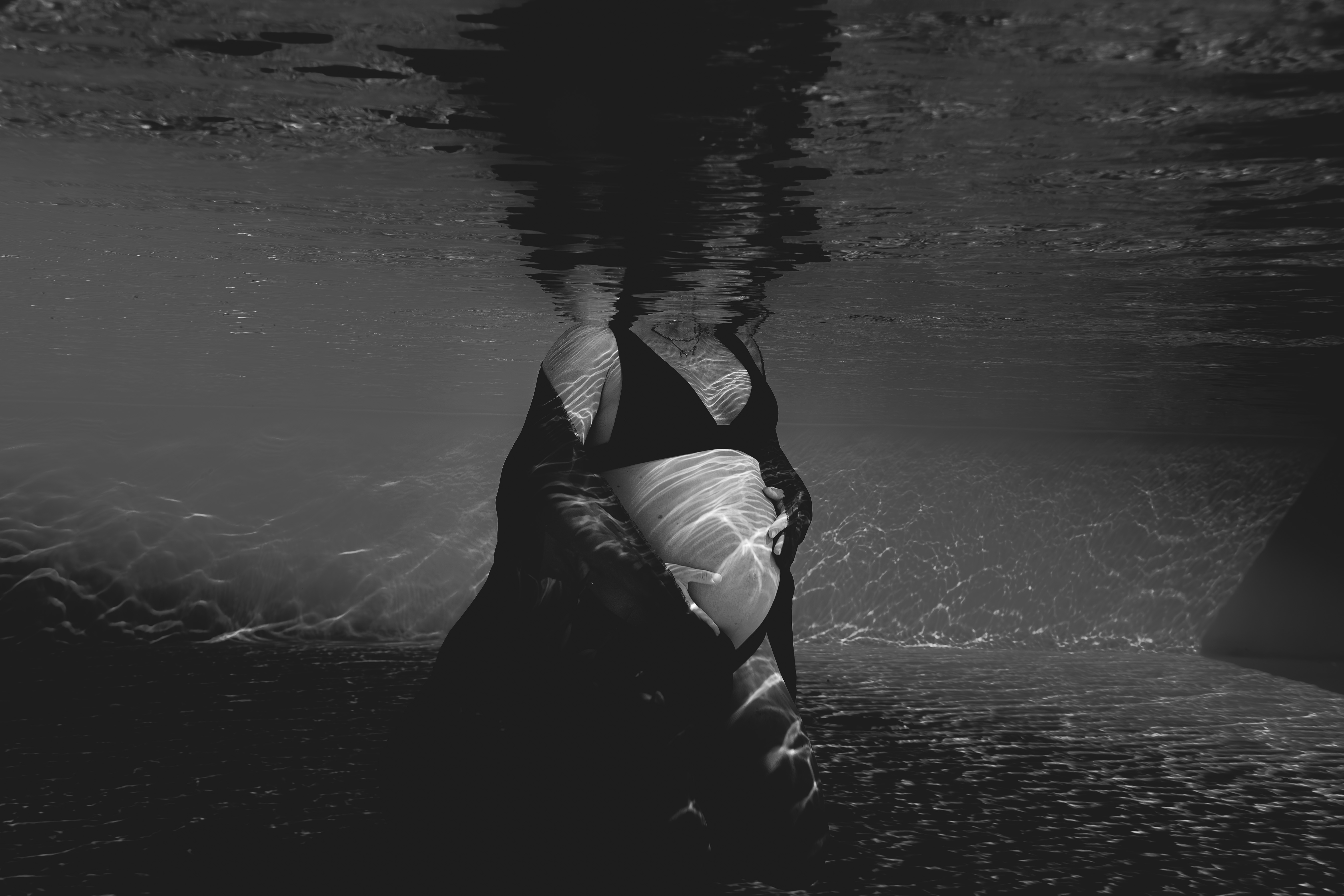 Future maman en apesanteur sous l'eau, lumière naturelle traversant la surface de la piscine — photographie grossesse aquatique